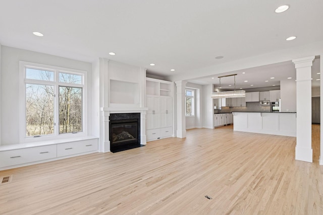 unfurnished living room featuring a fireplace, decorative columns, light wood finished floors, recessed lighting, and visible vents