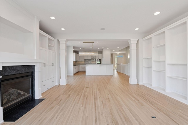 unfurnished living room featuring light wood-style floors, a high end fireplace, decorative columns, and recessed lighting