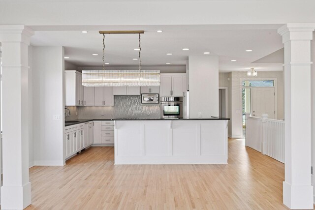 kitchen with decorative backsplash, light wood-style floors, dark countertops, stainless steel appliances, and ornate columns