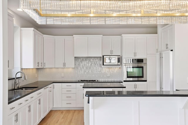 kitchen featuring dark countertops, light wood-style flooring, white cabinets, a sink, and built in appliances