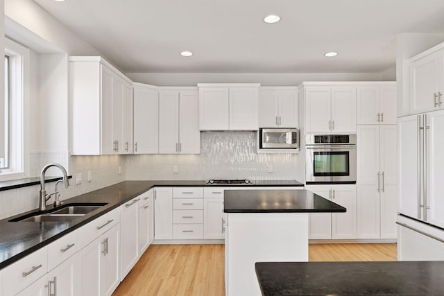 kitchen featuring light wood finished floors, tasteful backsplash, white cabinets, built in appliances, and a sink