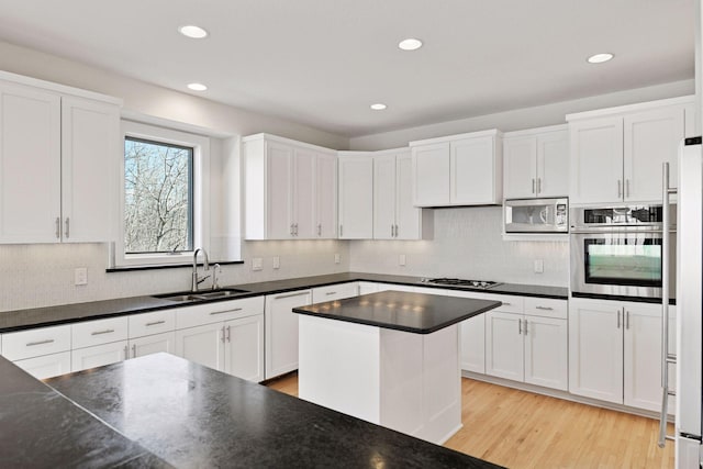 kitchen featuring stainless steel appliances, dark countertops, a sink, and white cabinetry