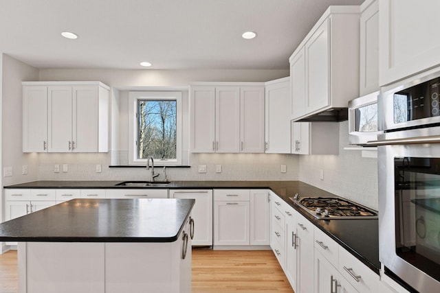 kitchen with light wood finished floors, dark countertops, appliances with stainless steel finishes, a healthy amount of sunlight, and a sink