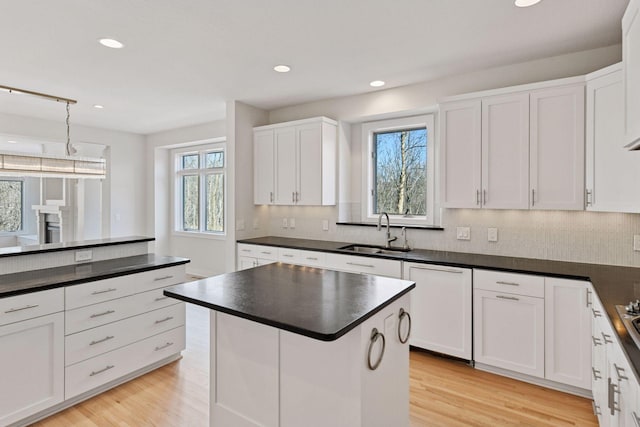 kitchen featuring dark countertops, white cabinets, a sink, and light wood-style flooring