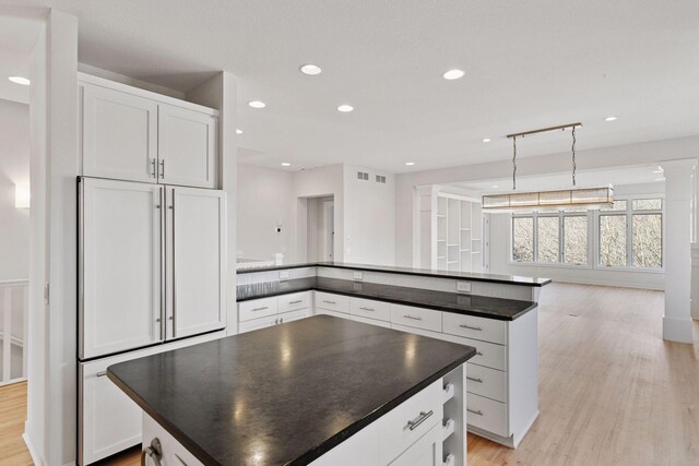 kitchen featuring paneled built in fridge, dark countertops, light wood-style flooring, and white cabinets