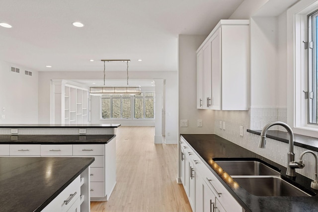 kitchen with a sink, visible vents, light wood-style floors, decorative backsplash, and dark countertops