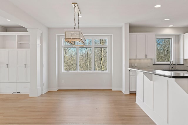 kitchen with decorative backsplash, light wood-style floors, white cabinetry, a sink, and baseboards