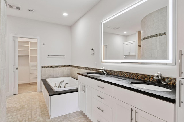 bathroom with a walk in closet, double vanity, a sink, and a bath