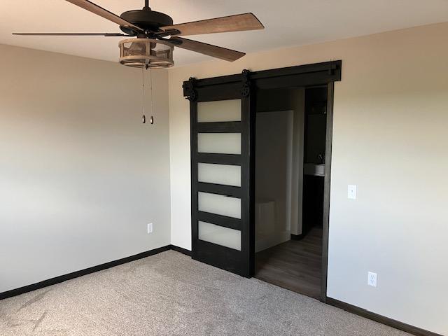 spare room featuring a barn door, carpet, baseboards, and ceiling fan