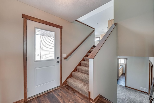 foyer entrance with wood finished floors, visible vents, baseboards, stairs, and a textured ceiling