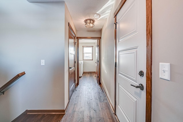 corridor featuring baseboards, a textured ceiling, an upstairs landing, and hardwood / wood-style flooring