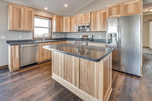 kitchen with dark countertops, light brown cabinetry, lofted ceiling, appliances with stainless steel finishes, and a sink