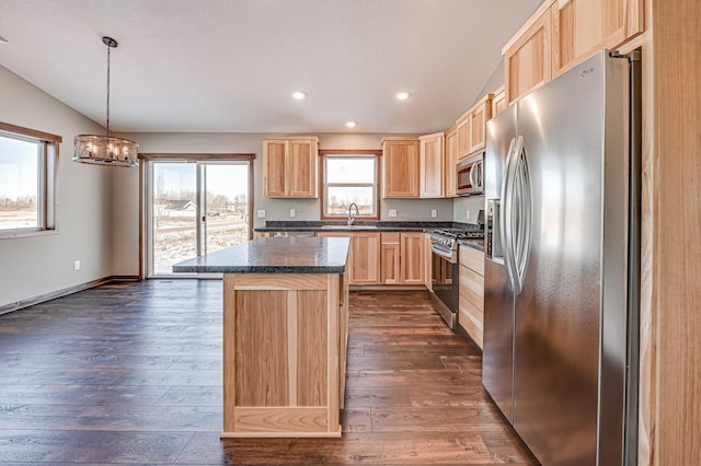 kitchen with light brown cabinets, dark countertops, a center island, stainless steel appliances, and dark wood-style flooring