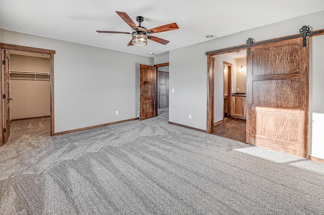 unfurnished bedroom with a barn door, carpet floors, baseboards, and a spacious closet