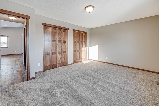 unfurnished bedroom with baseboards, multiple closets, a textured ceiling, and carpet flooring