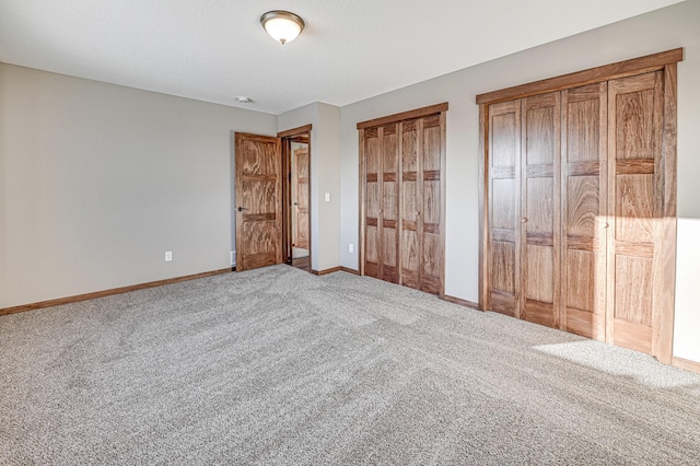 unfurnished bedroom featuring baseboards, multiple closets, and carpet floors