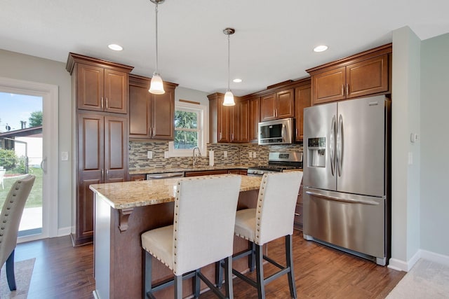 kitchen featuring a kitchen island, dark wood-style flooring, stainless steel appliances, hanging light fixtures, and tasteful backsplash