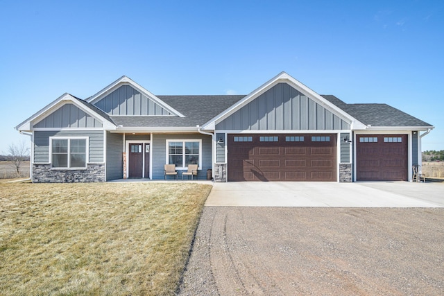 craftsman house featuring an attached garage, stone siding, driveway, a front lawn, and board and batten siding