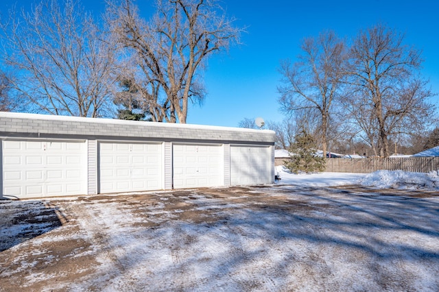 snow covered garage featuring fence