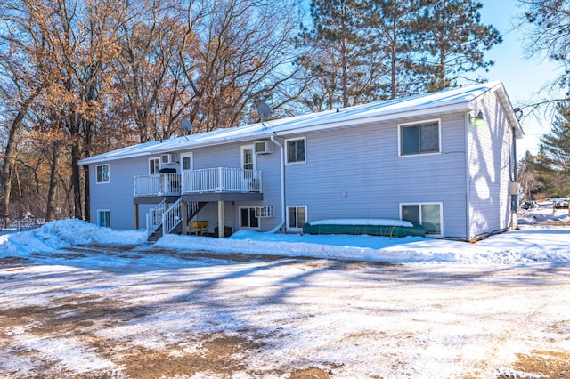 snow covered rear of property with an AC wall unit, a wooden deck, and stairs