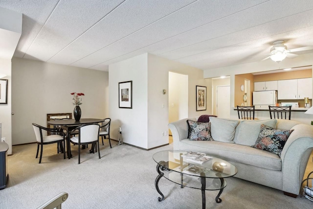 living room featuring light carpet, ceiling fan, baseboards, and a textured ceiling