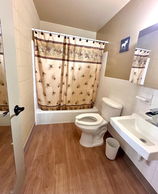 bathroom with tile walls, toilet, a shower with curtain, wood finished floors, and a sink