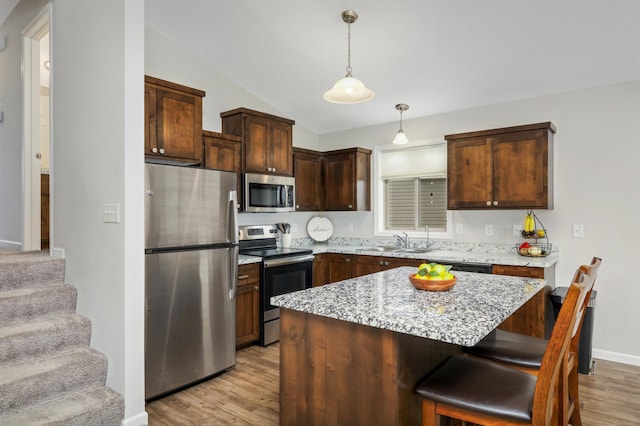 kitchen featuring stainless steel appliances, a sink, hanging light fixtures, and light wood finished floors