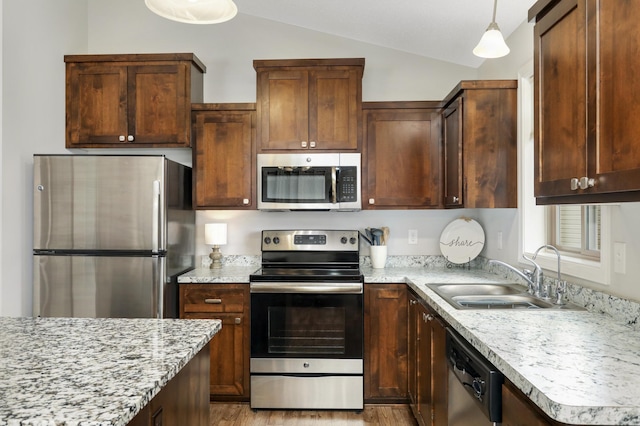 kitchen with lofted ceiling, stainless steel appliances, a sink, hanging light fixtures, and light wood finished floors