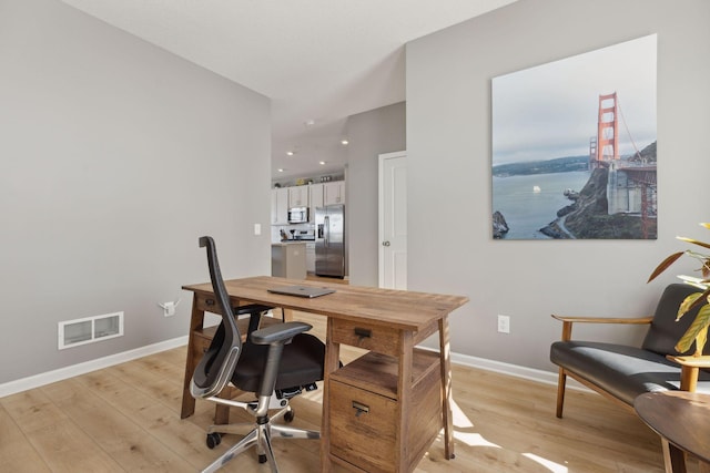 office area with light wood-type flooring, visible vents, and baseboards