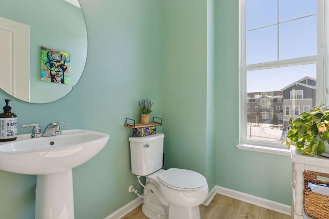 half bath featuring a sink, wood finished floors, toilet, and baseboards