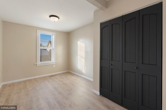 unfurnished bedroom featuring light wood finished floors, baseboards, and a closet