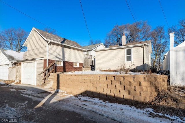 snow covered property with a garage, a chimney, and concrete driveway