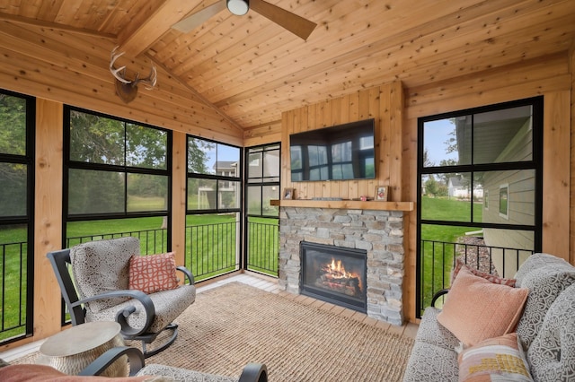 sunroom featuring lofted ceiling with beams, a stone fireplace, wood ceiling, and a ceiling fan