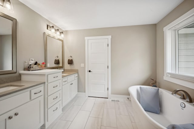 bathroom featuring double vanity, baseboards, visible vents, a soaking tub, and a sink