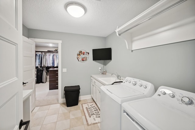 clothes washing area featuring cabinet space, washing machine and clothes dryer, a textured ceiling, a sink, and light tile patterned flooring