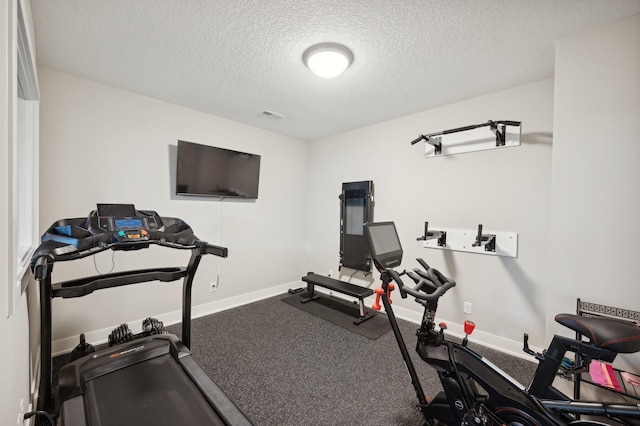 exercise room featuring visible vents, a textured ceiling, and baseboards