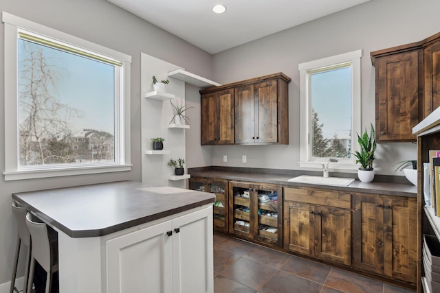 kitchen featuring dark countertops, dark tile patterned flooring, a sink, and dark brown cabinets