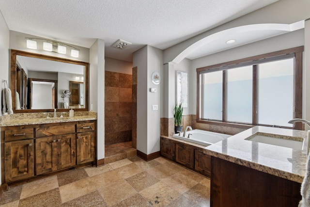 full bath with vanity, a textured ceiling, a bath, baseboards, and walk in shower