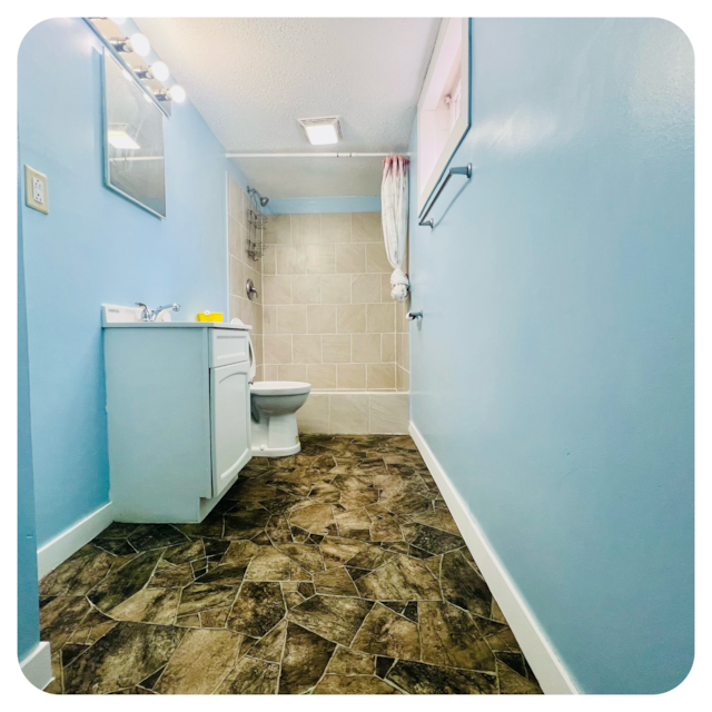 bathroom with baseboards, a shower with shower curtain, toilet, a textured ceiling, and vanity