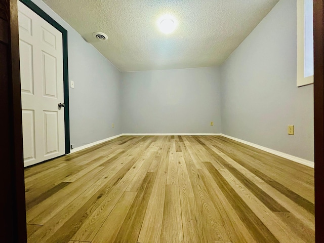 bonus room featuring a textured ceiling, visible vents, baseboards, vaulted ceiling, and light wood-type flooring