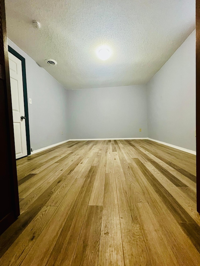 spare room with a textured ceiling, wood finished floors, visible vents, baseboards, and vaulted ceiling