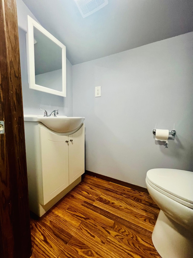 half bathroom featuring visible vents, toilet, vanity, wood finished floors, and baseboards