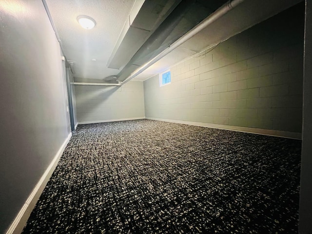 below grade area featuring concrete block wall, carpet floors, baseboards, and a textured ceiling