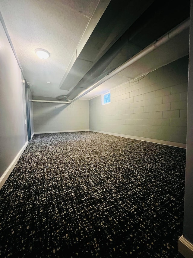 below grade area featuring concrete block wall, a textured ceiling, baseboards, and carpet flooring