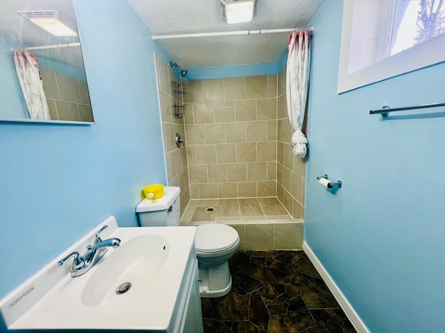 full bathroom with baseboards, tiled shower, toilet, a textured ceiling, and vanity