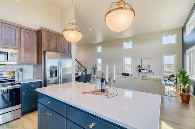 kitchen featuring stainless steel appliances, open floor plan, light countertops, and a kitchen island