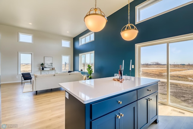 kitchen with light countertops, hanging light fixtures, open floor plan, a kitchen island, and blue cabinets