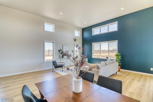 dining space featuring light wood finished floors, a high ceiling, baseboards, and recessed lighting