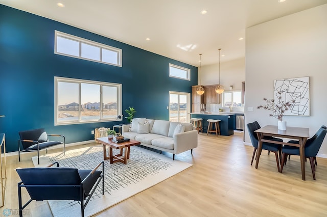 living room featuring recessed lighting, baseboards, light wood-style flooring, and a towering ceiling