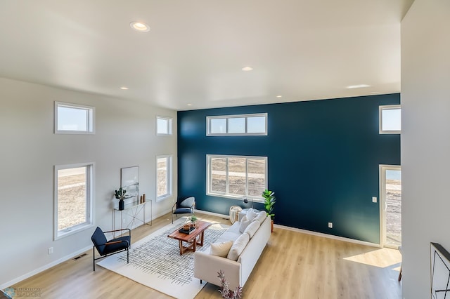 living room featuring light wood-style floors, visible vents, a towering ceiling, and baseboards